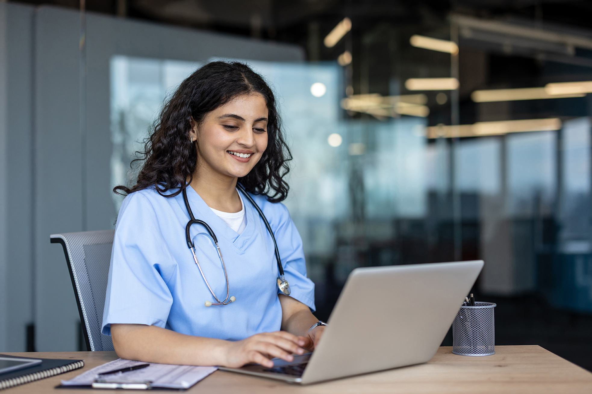 Woman wearing scrubs and stethoscope looking at laptop